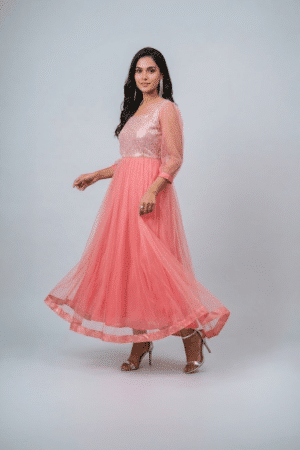 Woman wearing a coral pink shimmering tulle gown with a sequin bodice, square neckline and sheer three-quarter sleeves