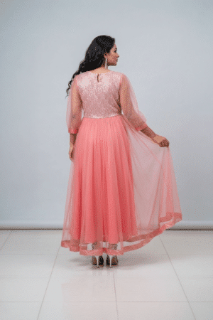 Woman wearing a coral pink shimmering tulle gown with a sequin bodice, square neckline and sheer three-quarter sleeves